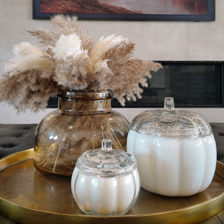 Decorative items including a vase with dried pampas grass and a white pumpkin-shaped candle on a gold tray.