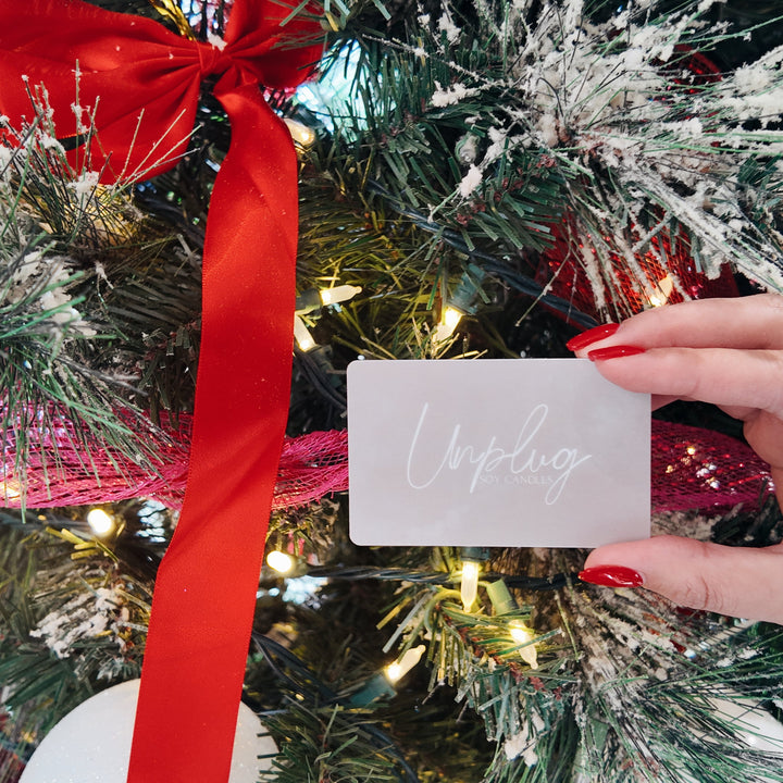 Hand holding a gift card in front of a decorated Christmas tree with red ribbons.