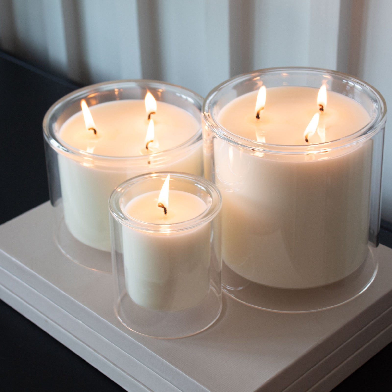 Three lit candles in clear glass holders on a white surface.