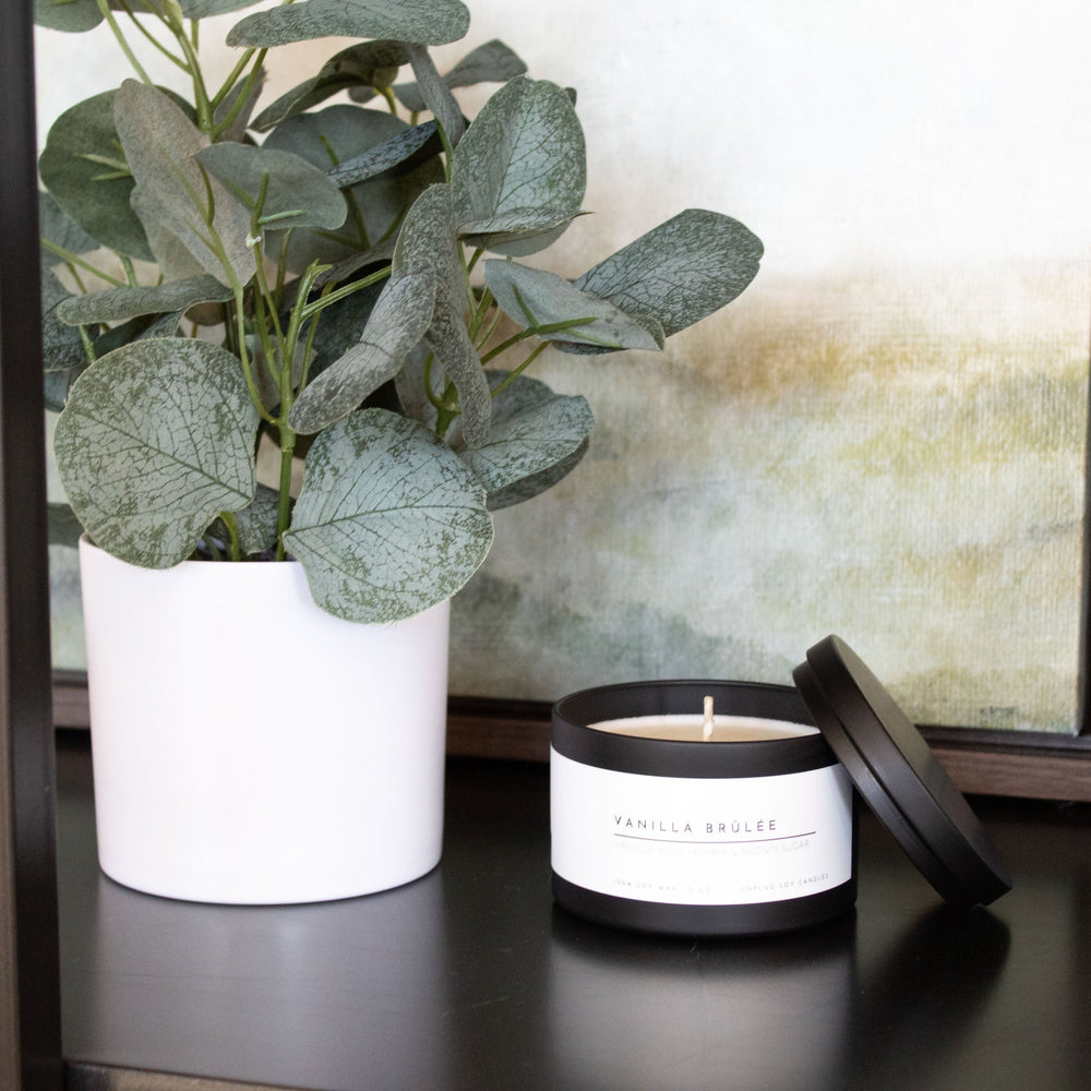 Candle with white label and plant on a reflective surface