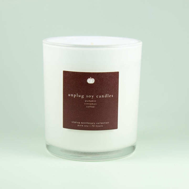 White soy candle with a chocolate brown label on a light gray background