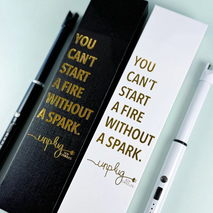 Two USB lighters, one with a black body and the other with a white body, both with gold text. The black lighter is in a black box and the white lighter is in a white box, both boxes have the text 'YOU CAN'T START A FIRE WITHOUT A SPARK'.